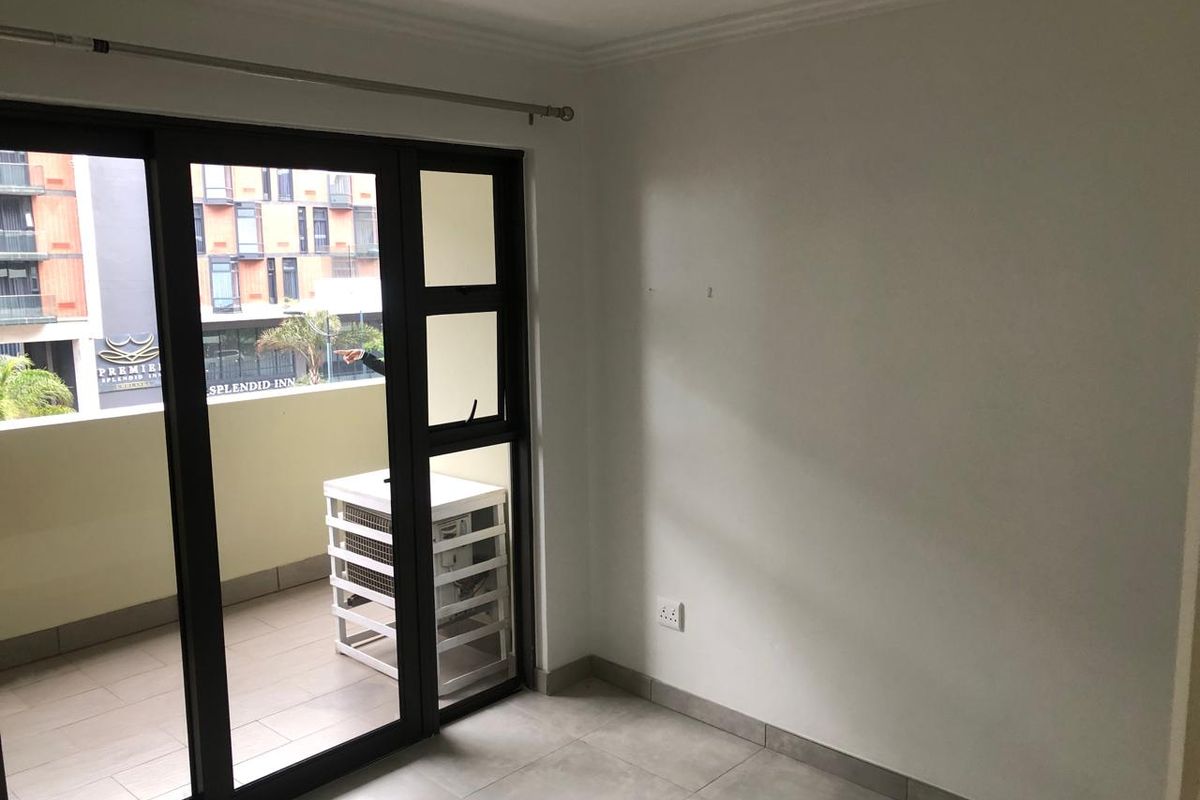 An empty bedroom featuring tiled flooring, neutral walls, and a sliding glass door providing access to a private balcony.