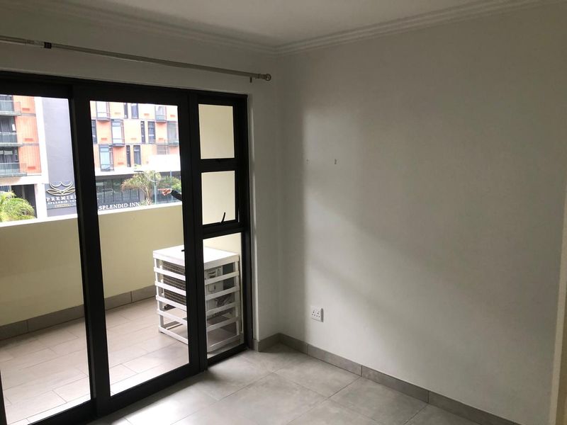 An empty bedroom featuring tiled flooring, neutral walls, and a sliding glass door providing access to a private balcony.