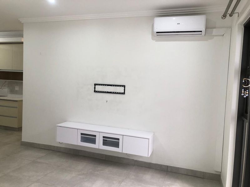 A bright, open-plan living area featuring tiled flooring, a wall-mounted media console, and a modern air conditioning unit.
