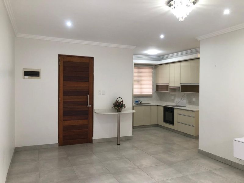 Modern open-plan living area featuring a sleek kitchen with integrated appliances, neutral tiled flooring, and a solid wood entrance door.