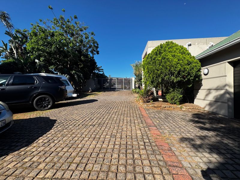 A paved driveway leading to a secure gated entrance with adjacent garage access and established garden landscaping.