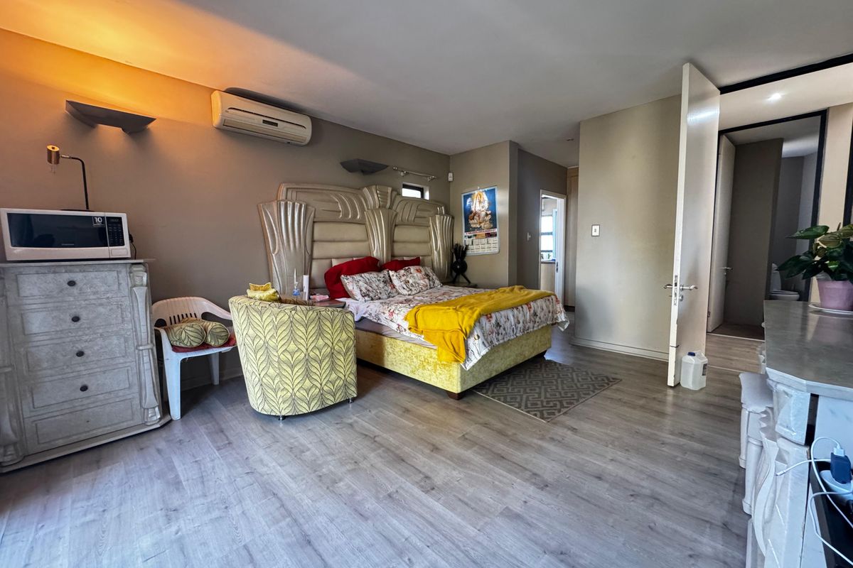 Spacious bedroom featuring light-toned laminate flooring, a wall-mounted air conditioning unit, and direct access to an adjoining room.