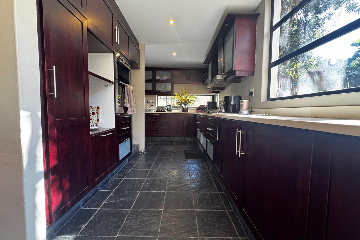 A galley-style kitchen featuring dark wood cabinetry, stone tile flooring, and a large window providing natural light.