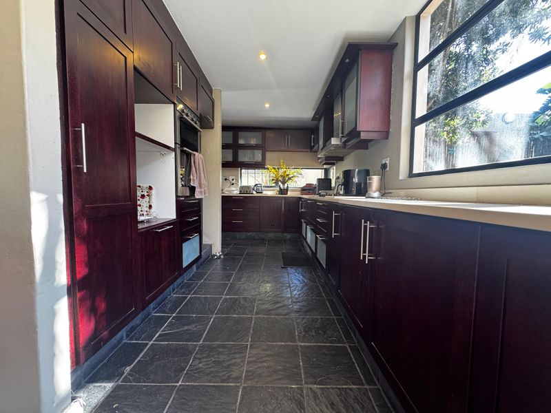 A galley-style kitchen featuring dark wood cabinetry, stone tile flooring, and a large window providing natural light.