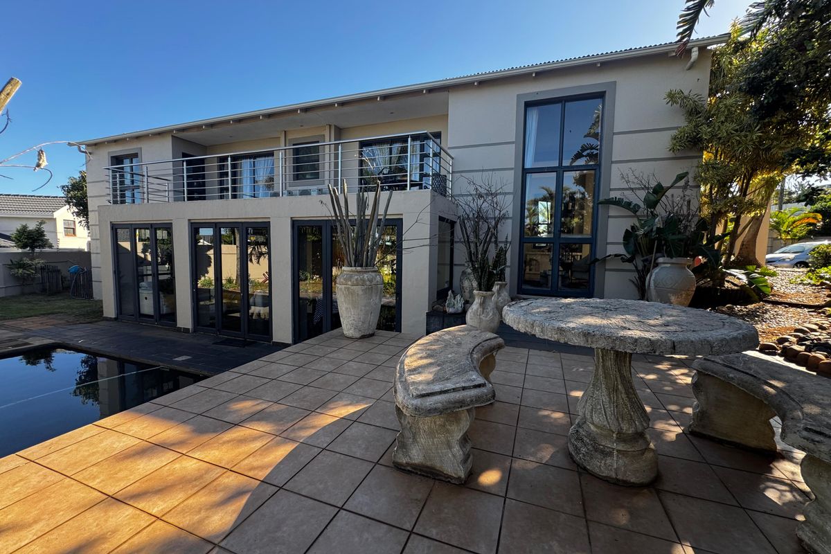 Rear exterior view featuring a tiled patio, swimming pool, and an upper-level balcony with modern aluminium fixtures and large windows.