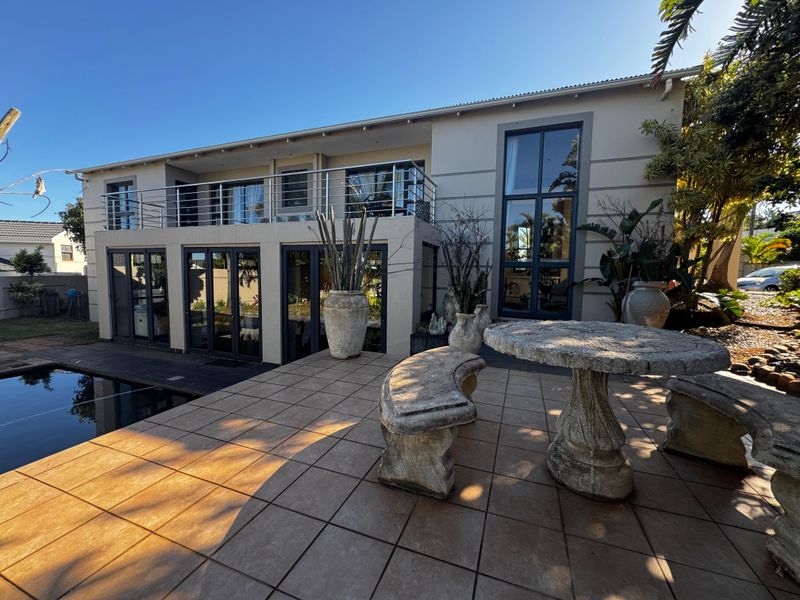 Rear exterior view featuring a tiled patio, swimming pool, and an upper-level balcony with modern aluminium fixtures and large windows.