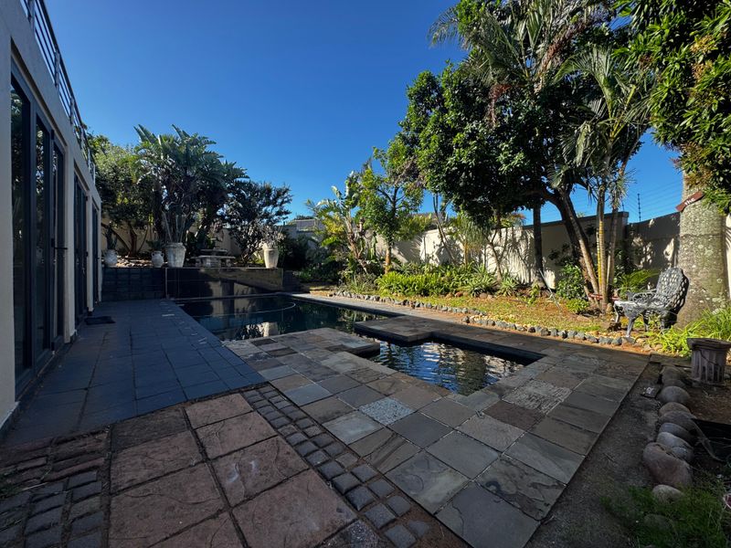 A well-maintained outdoor pool area featuring stone paving, a swimming pool, and established garden landscaping, providing a private and tranquil backyard setting.