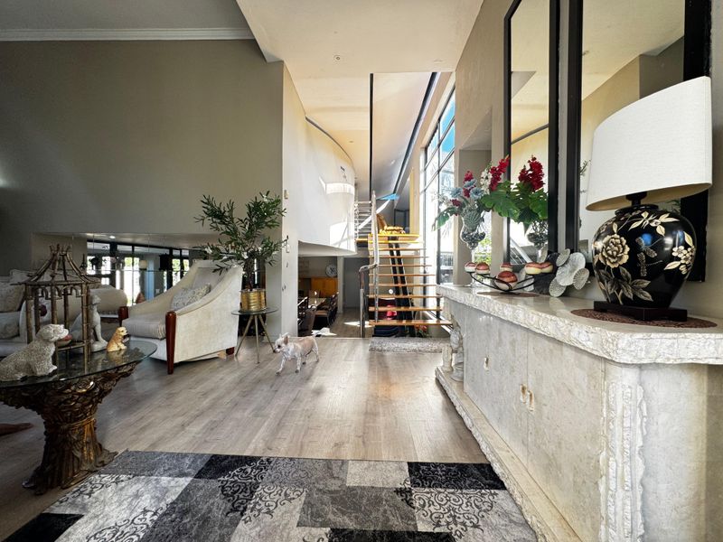Spacious open-plan living area featuring modern laminate flooring, an elegant open-tread staircase with stainless steel railings, and abundant natural light from large windows.