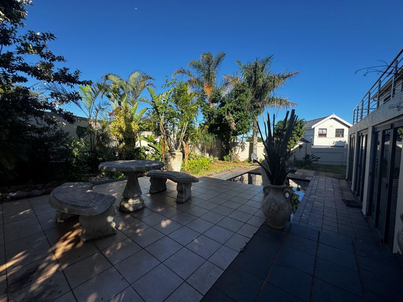 Outdoor entertainment area featuring a tiled patio, swimming pool, and established garden landscaping, adjacent to the main house structure.