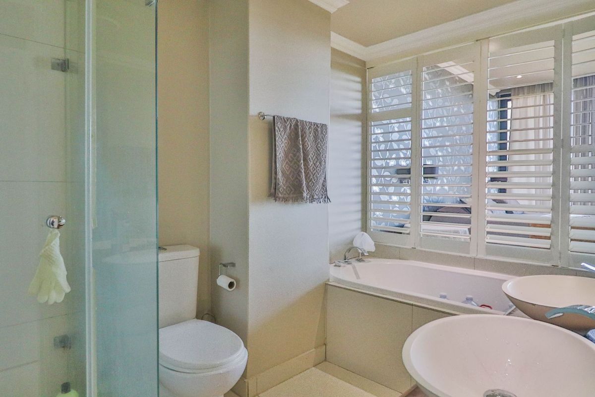 Modern bathroom featuring a glass shower enclosure, built-in bathtub, dual vessel sinks, and elegant plantation shutters for natural light control.