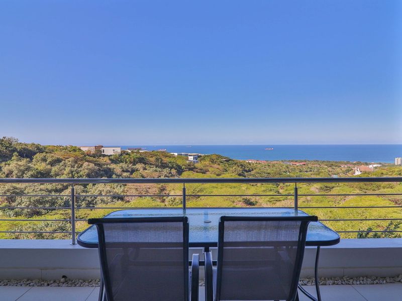 A spacious balcony featuring a modern stainless steel balustrade and tiled flooring, offering expansive panoramic views of the surrounding landscape and the ocean.