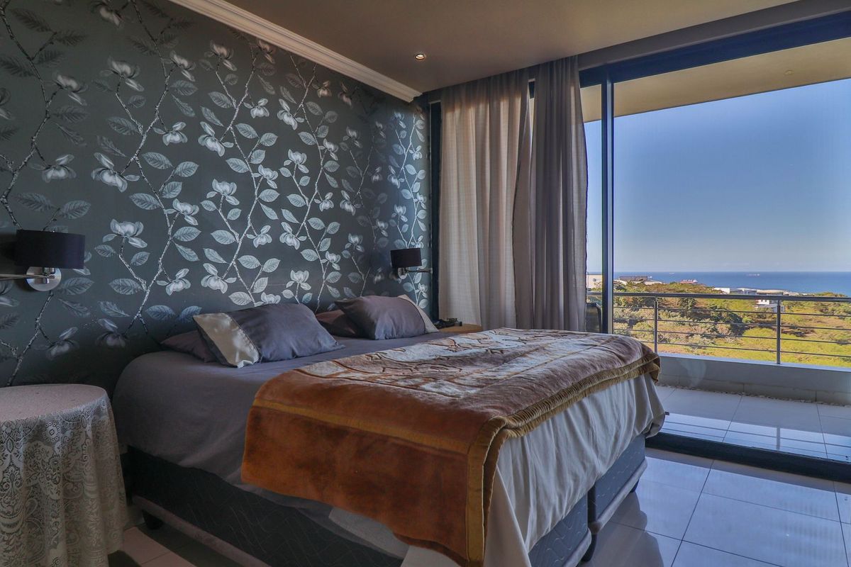 A well-maintained bedroom featuring patterned wallpaper, tiled flooring, and a large sliding glass door providing access to a balcony with scenic ocean views.