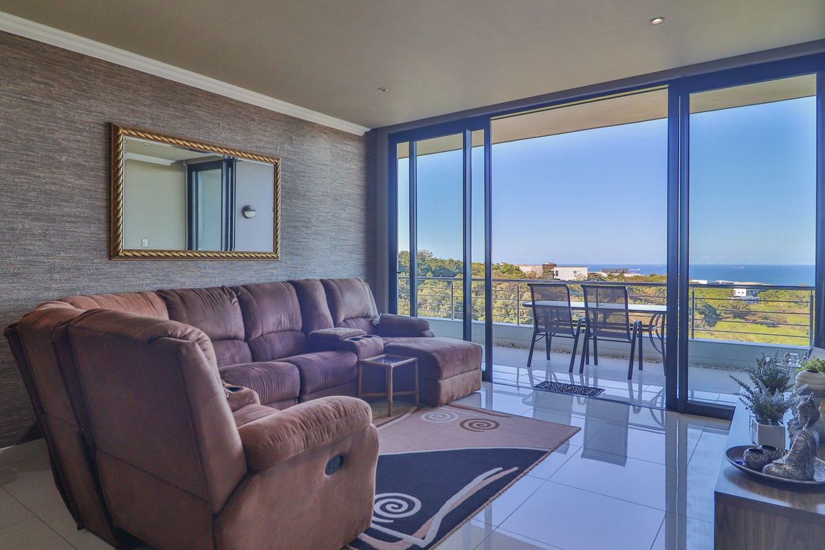 Spacious living room featuring large sliding glass doors that open to a balcony with scenic coastal views, complemented by modern tiled flooring.
