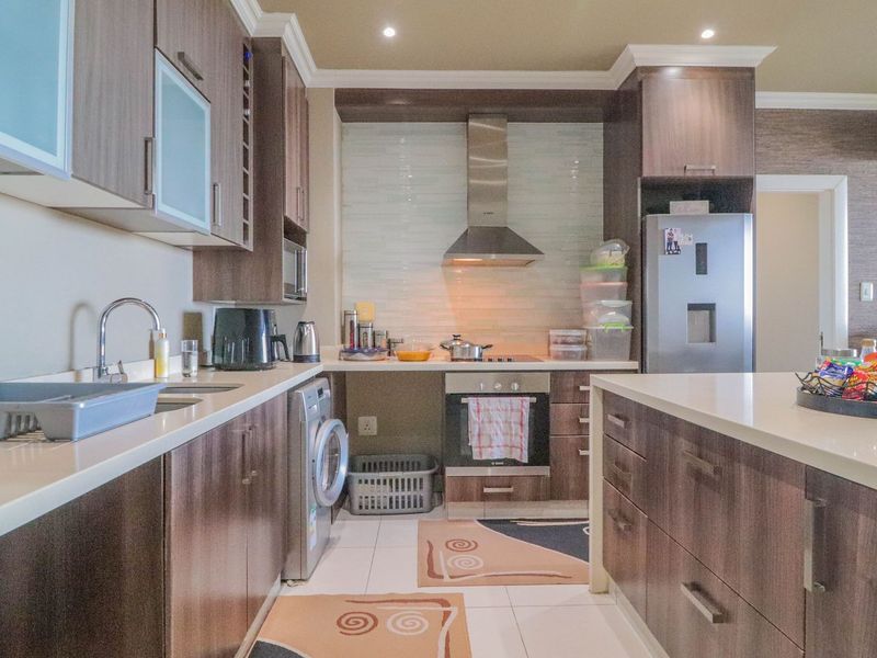 Modern kitchen featuring dark wood cabinetry, stone countertops, integrated stainless steel appliances, and tiled flooring with recessed lighting.