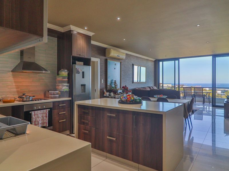Modern open-plan kitchen and living area featuring sleek cabinetry, stone countertops, and large sliding doors leading to a balcony with ocean views.