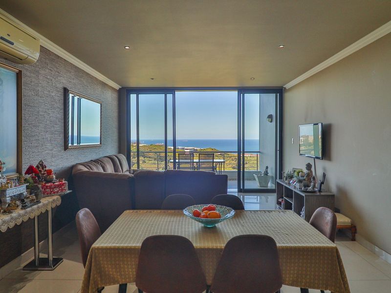Spacious open-plan living and dining area featuring tiled floors, recessed lighting, and large sliding doors opening to a balcony with scenic ocean views.