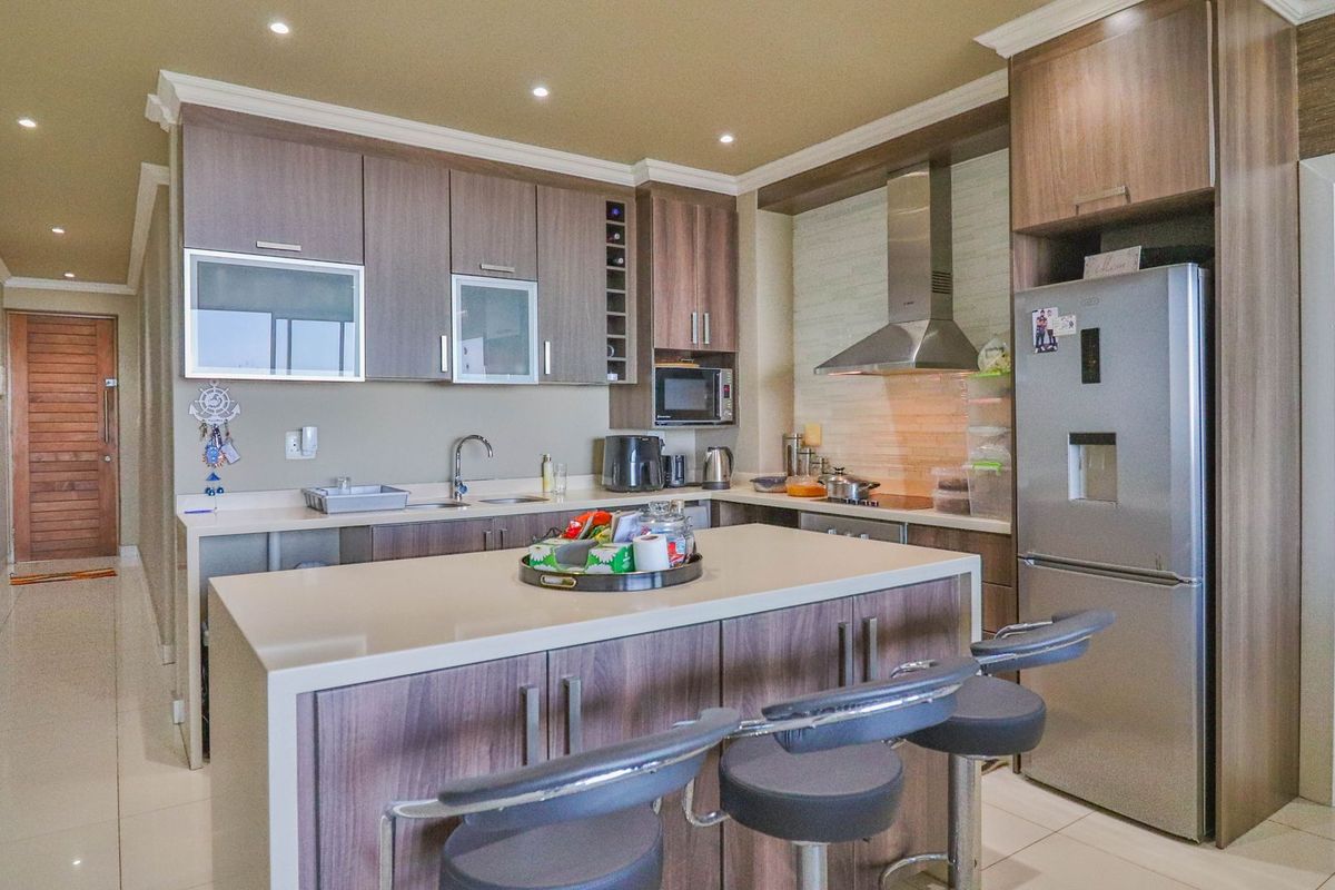 Modern kitchen featuring wood-finish cabinetry, stone countertops, a central island with breakfast bar seating, and integrated stainless steel appliances.