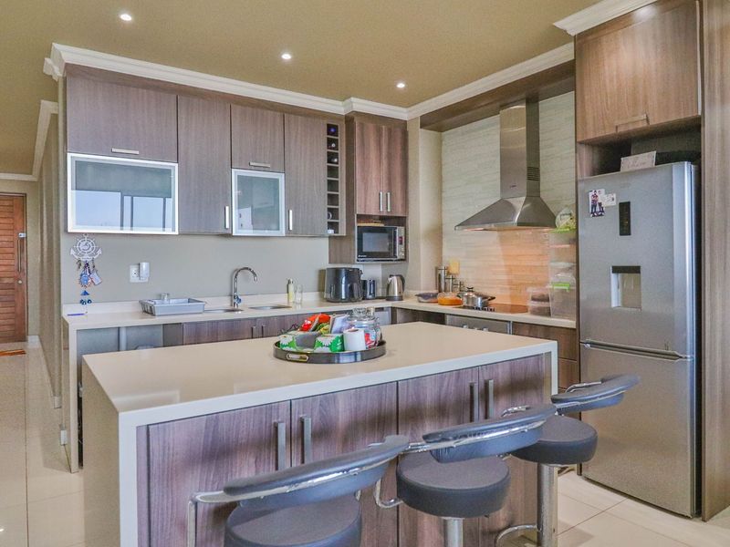 Modern kitchen featuring wood-finish cabinetry, stone countertops, a central island with breakfast bar seating, and integrated stainless steel appliances.