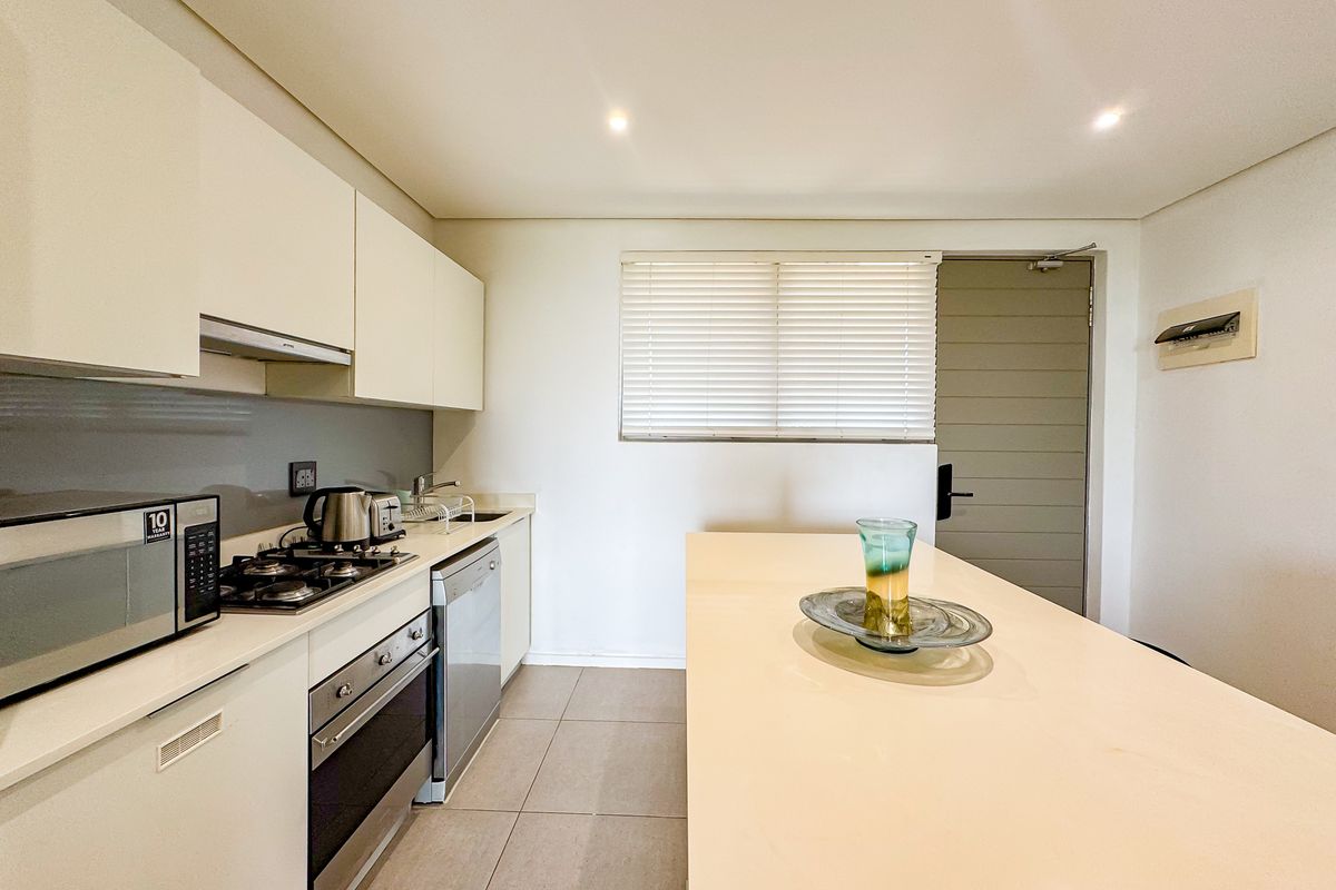 Modern kitchen featuring sleek white cabinetry, stone countertops, a gas hob, integrated appliances, and a central island, finished with neutral floor tiles.