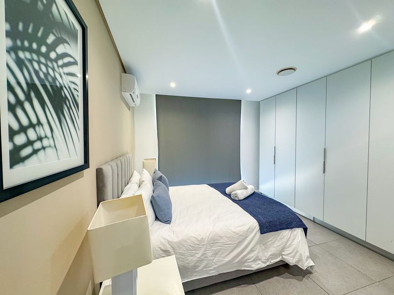 Modern bedroom featuring extensive built-in wardrobes, tiled flooring, recessed lighting, and a wall-mounted split-system air conditioner.