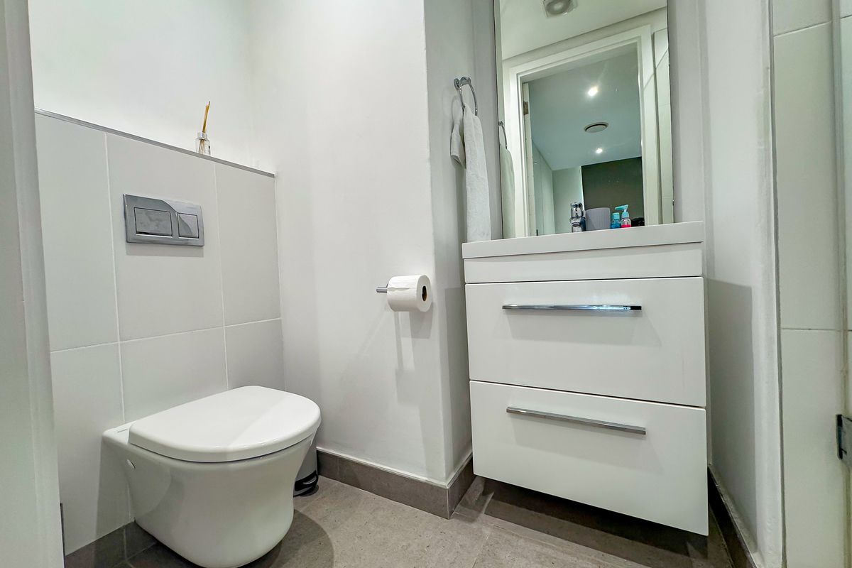 Modern bathroom featuring a wall-hung toilet with concealed cistern, a sleek white vanity cabinet with basin, and neutral floor-to-ceiling tiling.