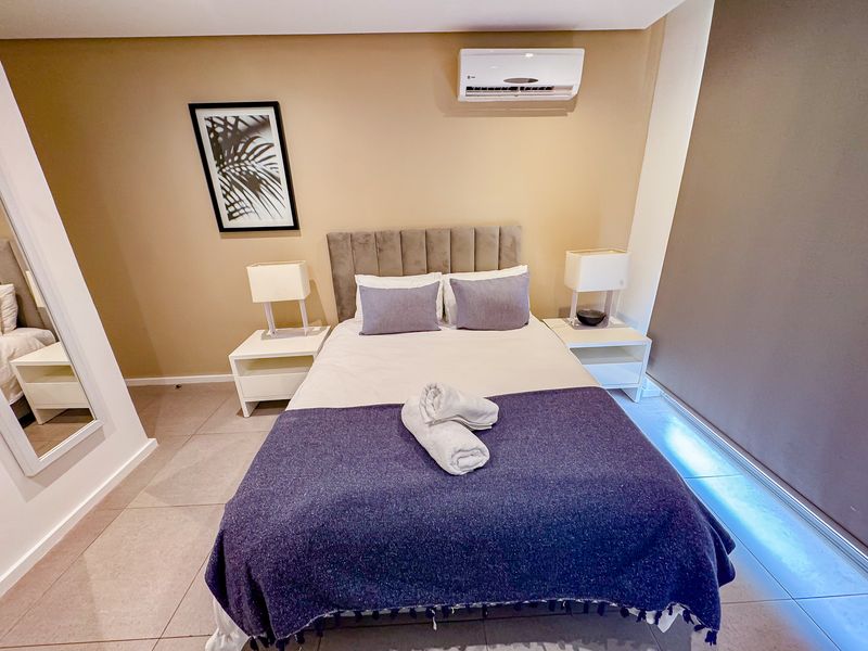 A well-maintained bedroom featuring tiled flooring, a neutral color palette, and a wall-mounted split-system air conditioning unit.