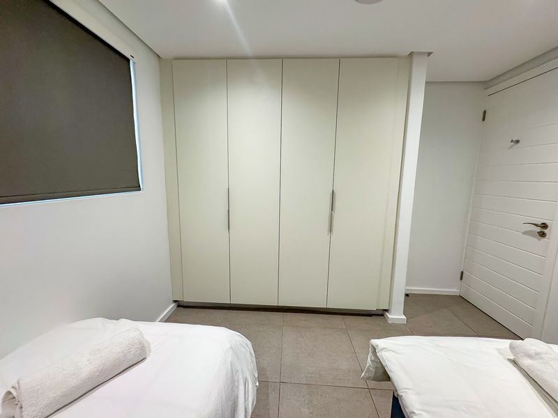 A clean and well-maintained bedroom featuring neutral tiled flooring, a large built-in wardrobe, and a modern roller blind.