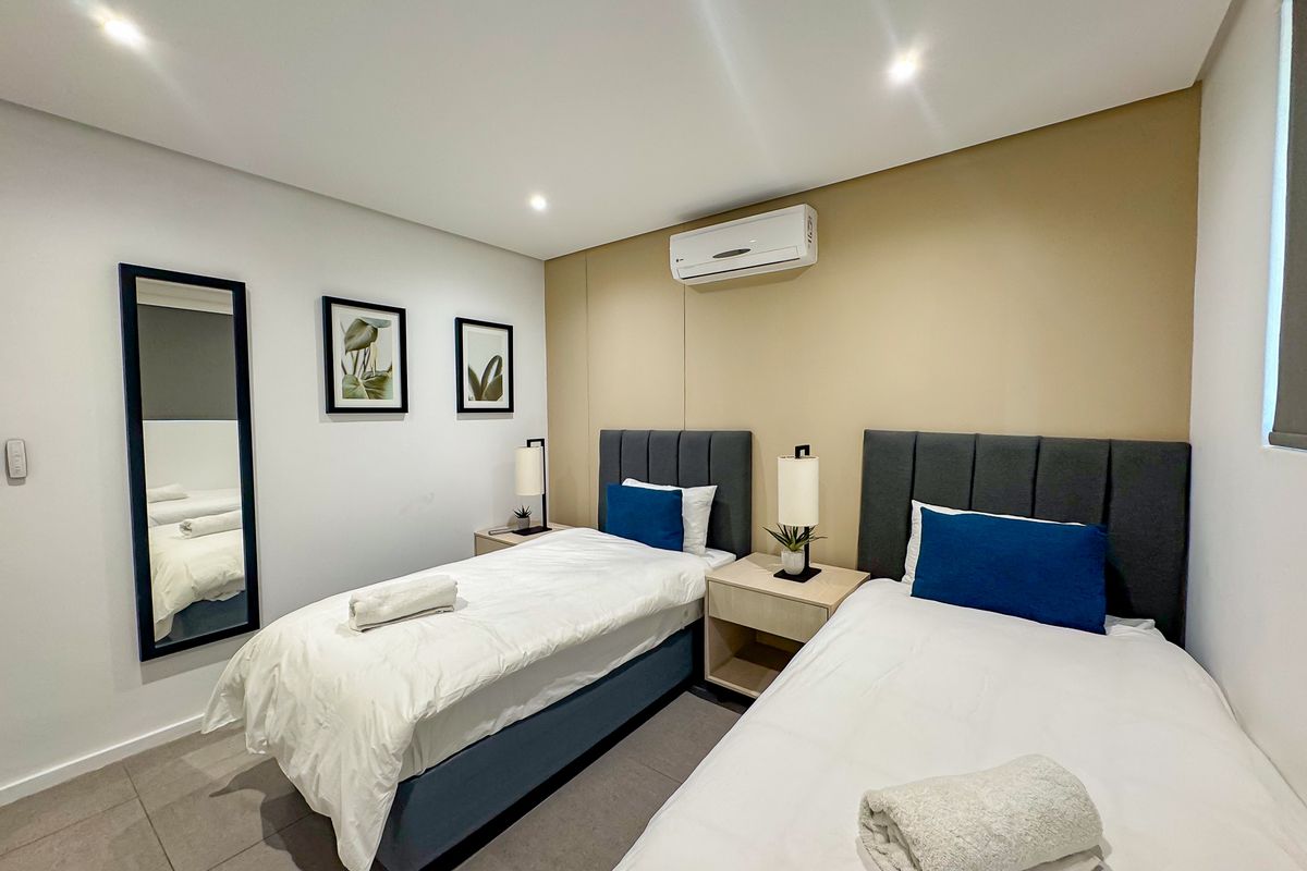 A modern, well-maintained bedroom featuring tiled flooring, recessed downlighting, and a wall-mounted air conditioning unit.