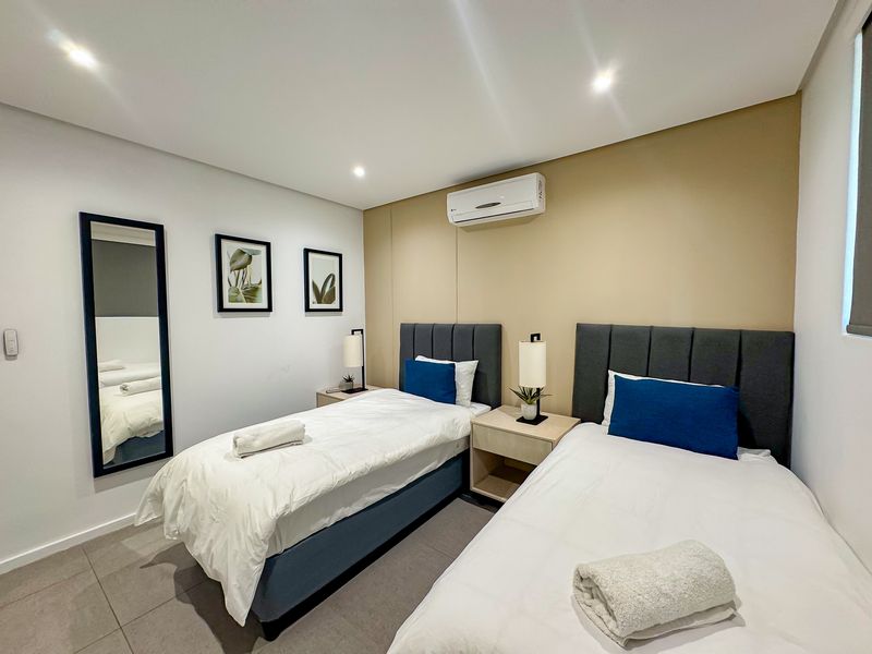 A modern, well-maintained bedroom featuring tiled flooring, recessed downlighting, and a wall-mounted air conditioning unit.