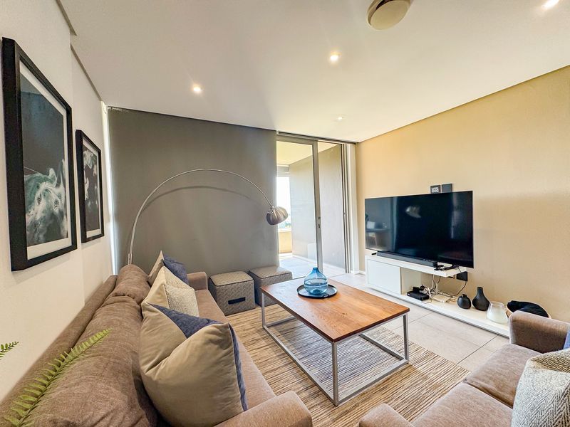 A well-lit living room featuring tiled flooring, recessed downlighting, and a sliding glass door providing access to the balcony.