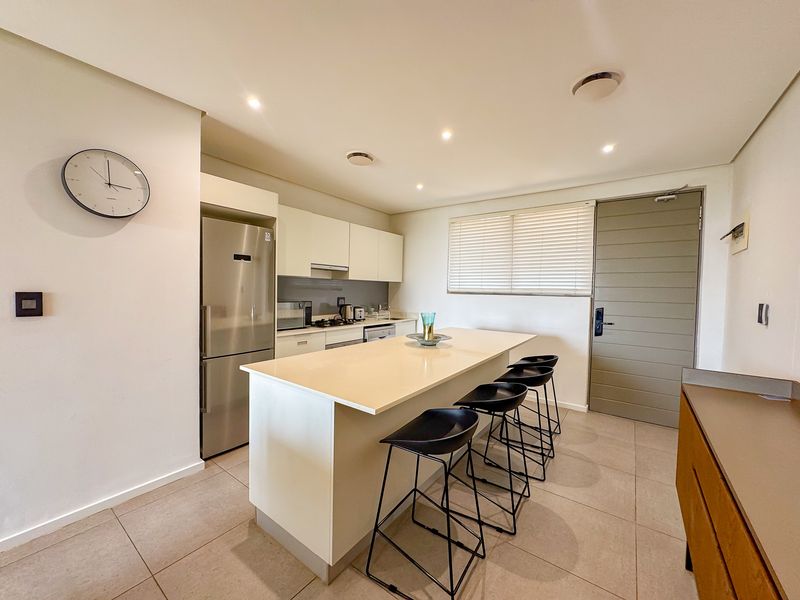 Modern kitchen featuring a central island, sleek cabinetry, recessed lighting, and neutral tiled flooring, creating a clean and functional culinary space.