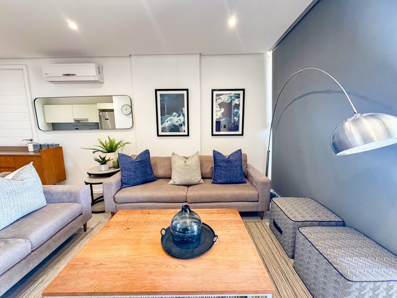 A well-maintained living room featuring recessed downlighting, a split-system air conditioner, and a modern accent wall.