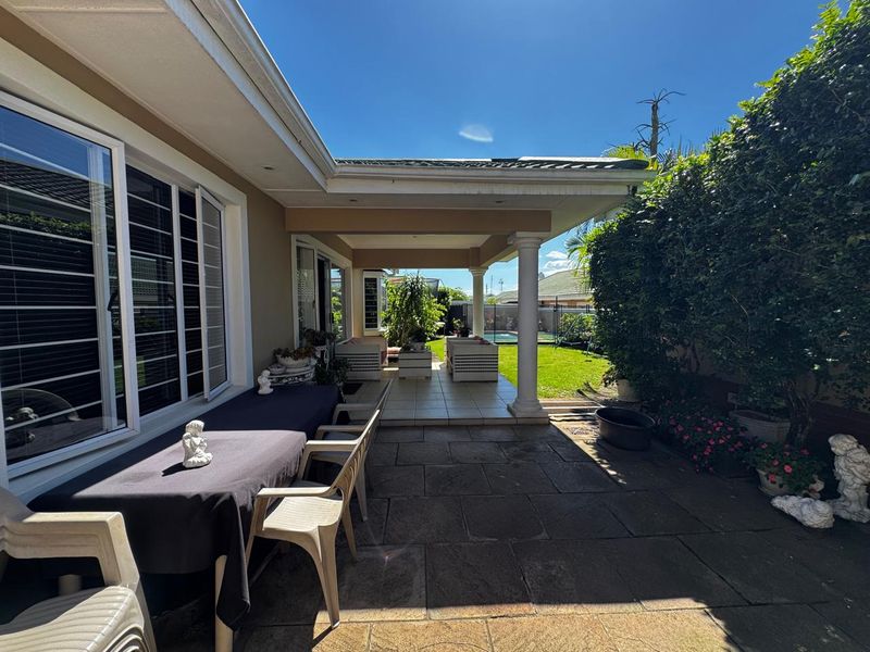 A spacious covered patio area featuring tiled flooring, structural columns, and recessed lighting, seamlessly transitioning to an outdoor stone-paved garden space.