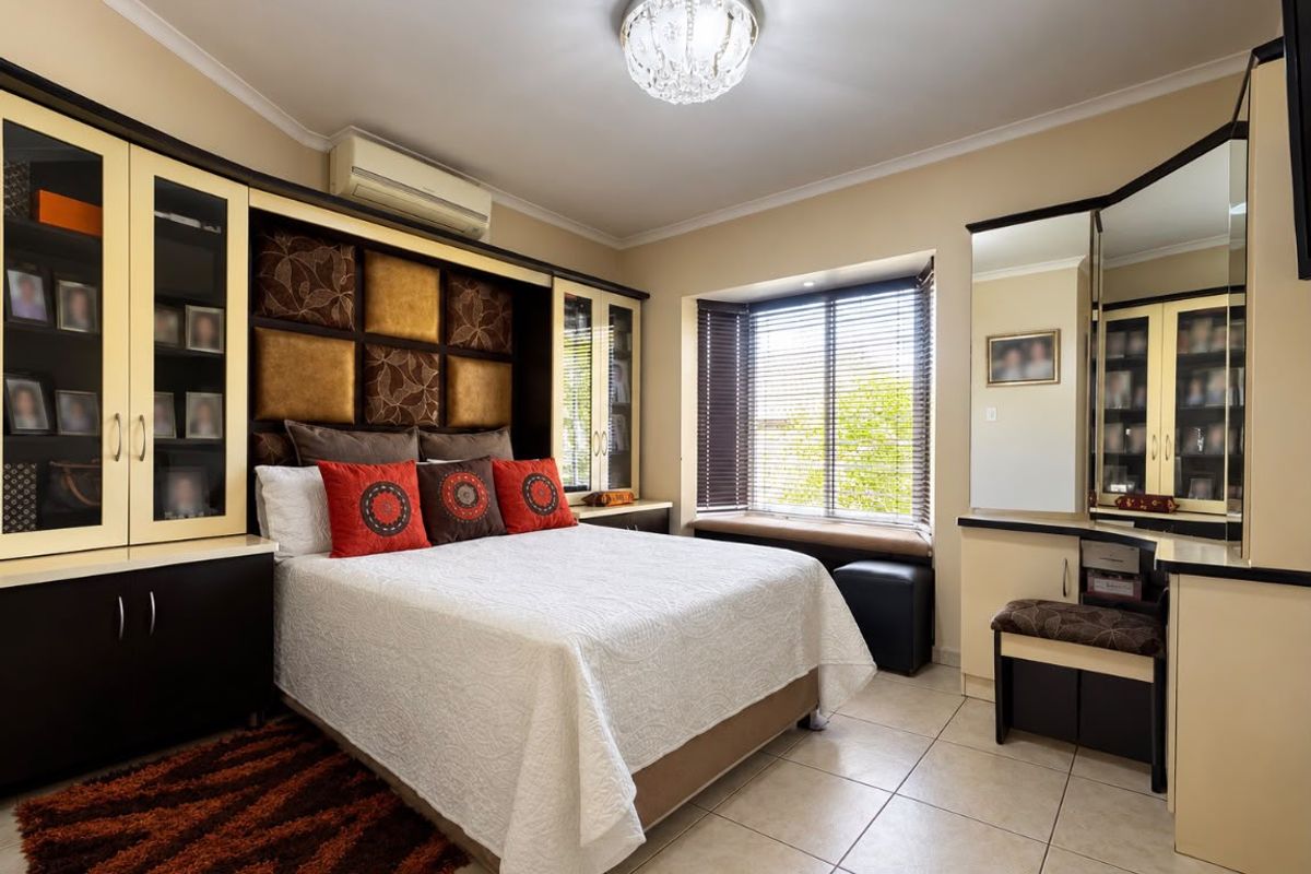 Well-appointed bedroom featuring extensive built-in cabinetry, a dedicated vanity area, split-system air conditioning, and a charming bay window with integrated seating.