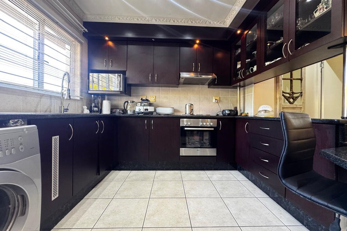 A functional kitchen featuring dark wood cabinetry, granite countertops, built-in oven, extractor fan, and tiled flooring with a classic coved ceiling finish.