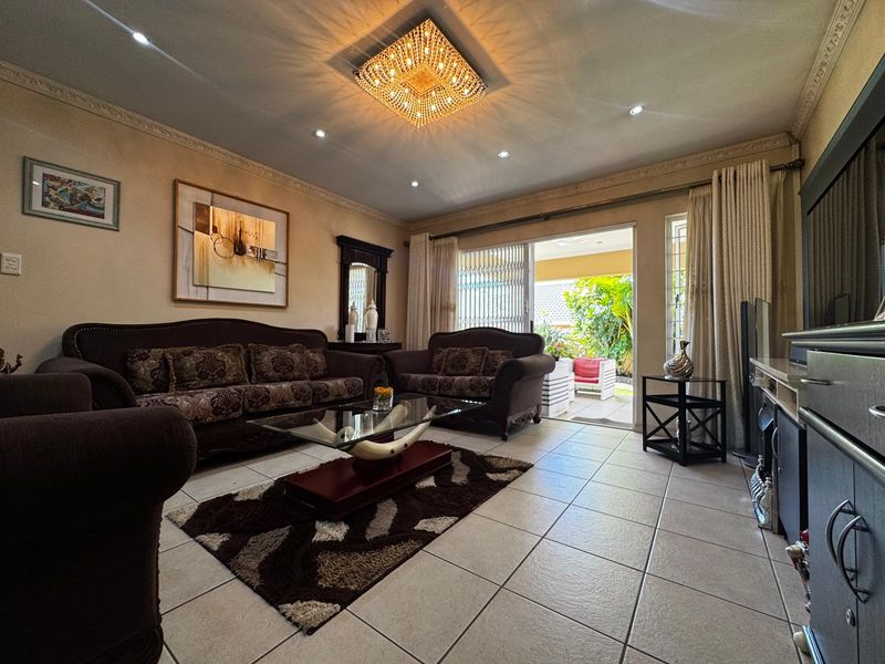 A well-maintained living room featuring tiled flooring, decorative ceiling cornices, and direct access to an outdoor patio through sliding glass doors.