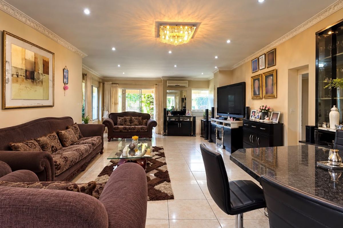 Spacious living room featuring tiled flooring, decorative crown molding, recessed lighting, and a central crystal chandelier, with access to the outdoor area.
