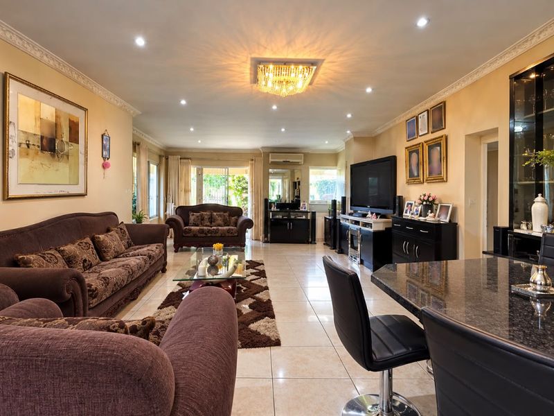 Spacious living room featuring tiled flooring, decorative crown molding, recessed lighting, and a central crystal chandelier, with access to the outdoor area.