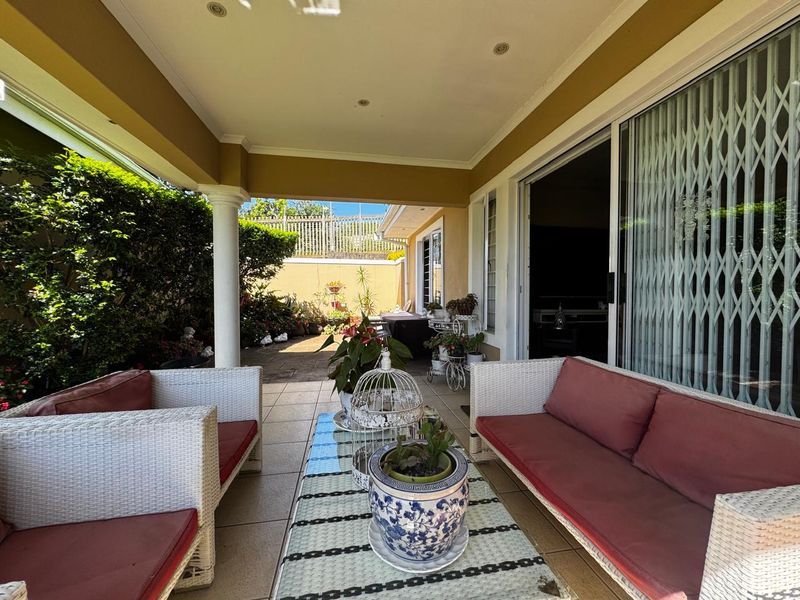 A covered patio area featuring tiled flooring, recessed lighting, and sliding glass doors with security gates, providing access to the garden.