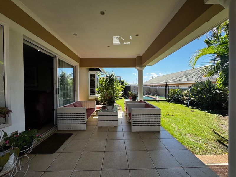 A covered patio area featuring tiled flooring, recessed lighting, and direct access to the garden and pool area through sliding glass doors.