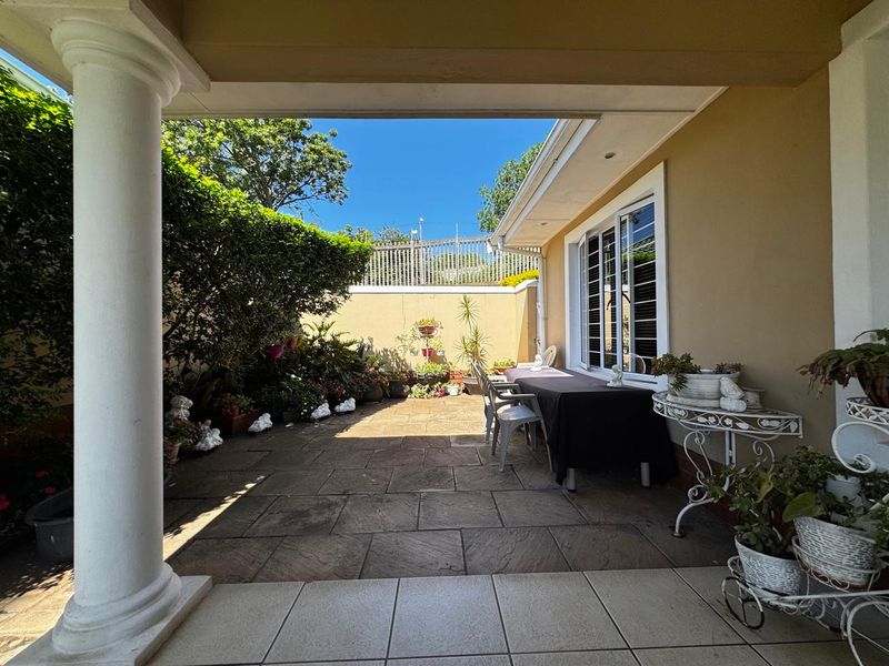 A covered patio area featuring stone paving, a classical column, and direct access to the garden through sliding glass doors.