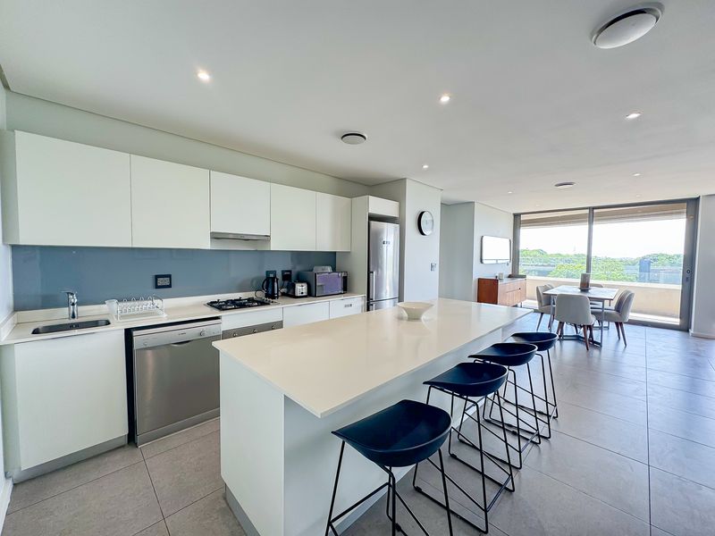 Modern open-plan kitchen featuring a large island, quartz countertops, integrated appliances, and seamless flow to the dining area and balcony with natural light.