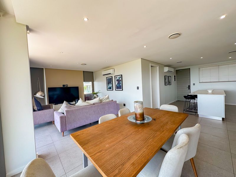 Spacious open-plan living, dining, and kitchen area featuring modern tiled flooring, recessed lighting, and dual air conditioning units in a well-maintained apartment setting.