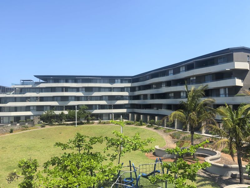 A view of a modern multi-story apartment complex featuring private balconies overlooking a well-maintained communal garden and landscaped grounds.