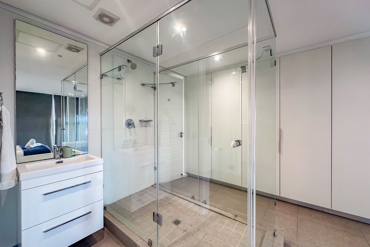 Modern bathroom featuring a spacious glass-enclosed walk-in shower, wall-mounted vanity with integrated basin, and ample built-in storage cabinetry.