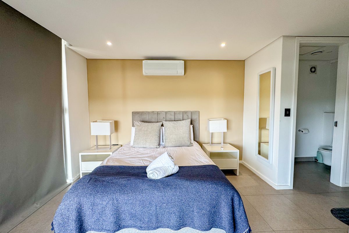 A well-maintained bedroom featuring tiled flooring, recessed lighting, a wall-mounted air conditioning unit, and direct access to an en-suite bathroom.