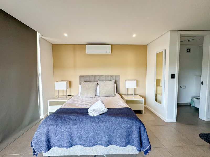 A well-maintained bedroom featuring tiled flooring, recessed lighting, a wall-mounted air conditioning unit, and direct access to an en-suite bathroom.