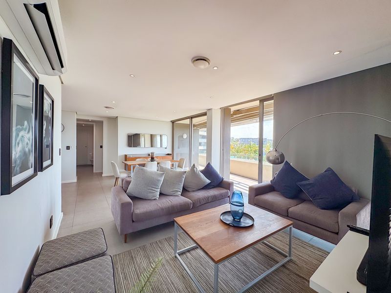 Spacious open-plan living and dining area featuring tiled floors, recessed lighting, a split-system air conditioner, and large sliding doors leading to a balcony.