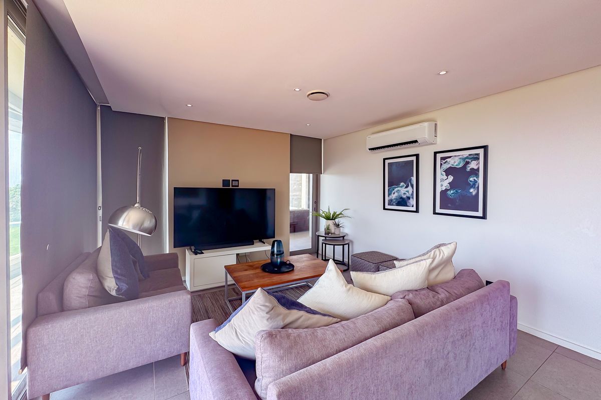 A well-maintained living room featuring tiled flooring, recessed downlighting, and a wall-mounted split-system air conditioner.