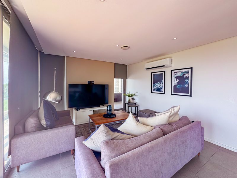 A well-maintained living room featuring tiled flooring, recessed downlighting, and a wall-mounted split-system air conditioner.
